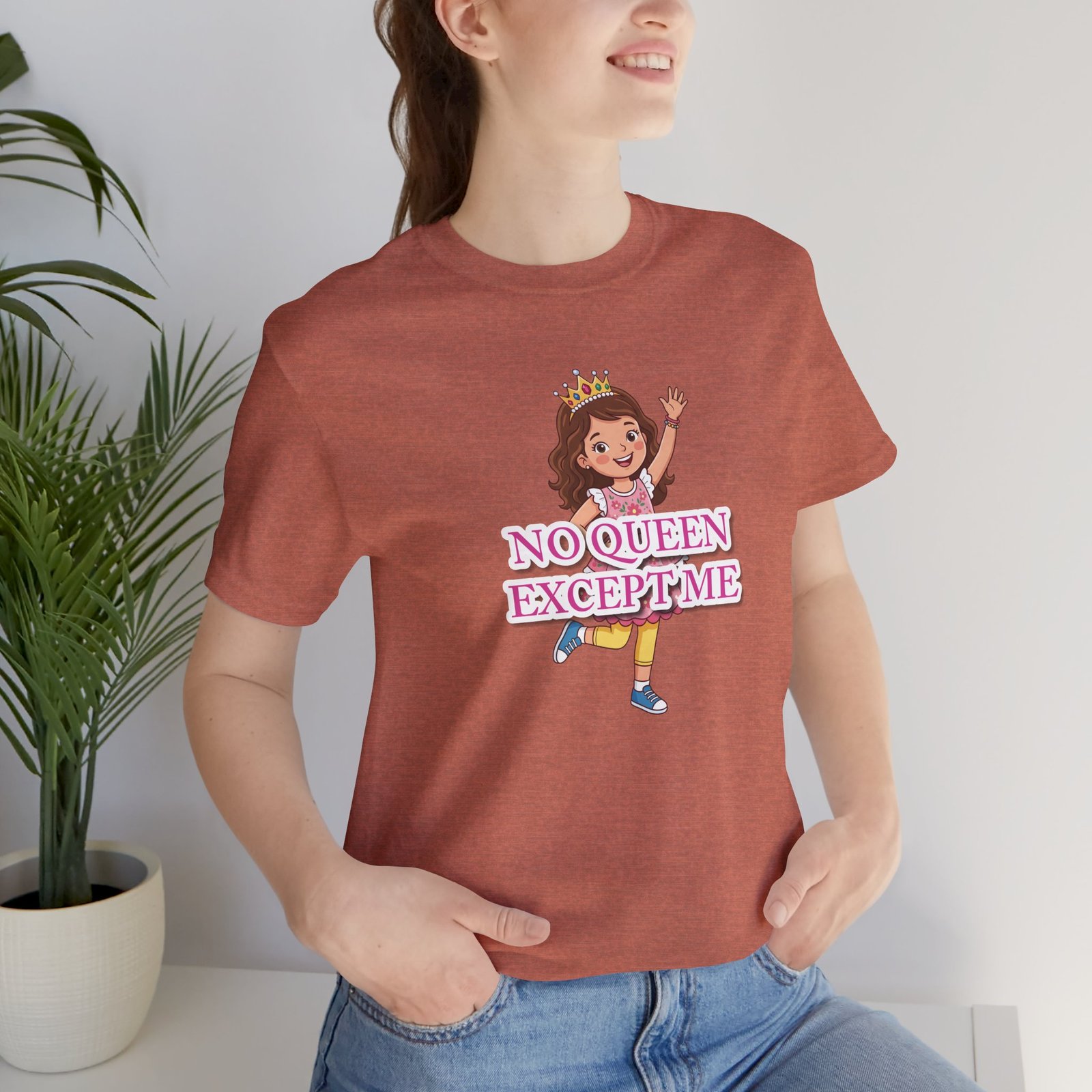 A girl wearing a pink No Queen Except Me Tee featuring a whimsical illustration of a confident little queen with a crown.