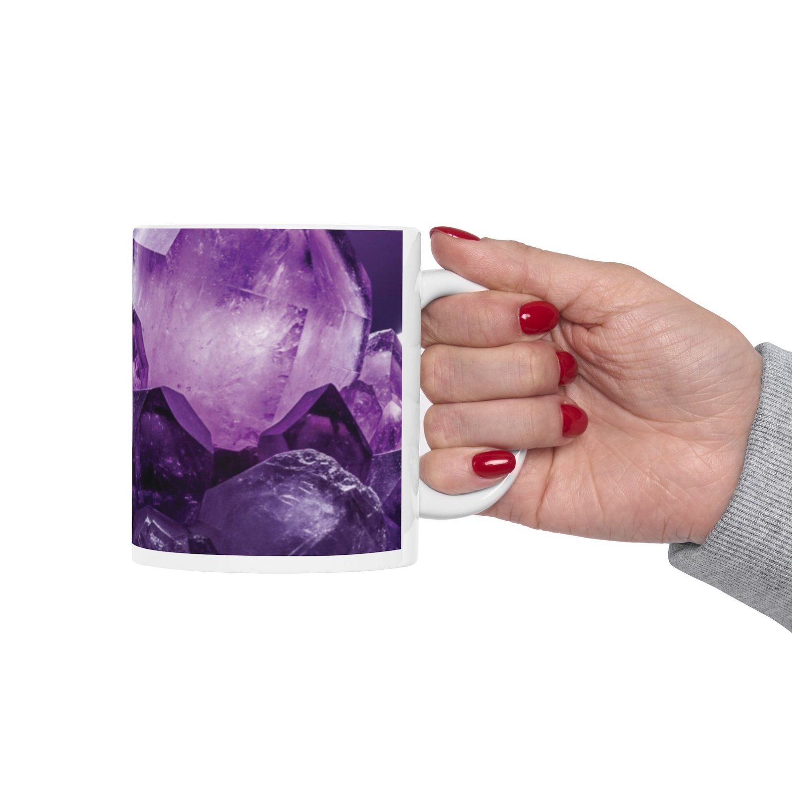 A hand holding a white ceramic mug decorated with a vibrant, close-up amethyst crystal pattern in deep purple tones.