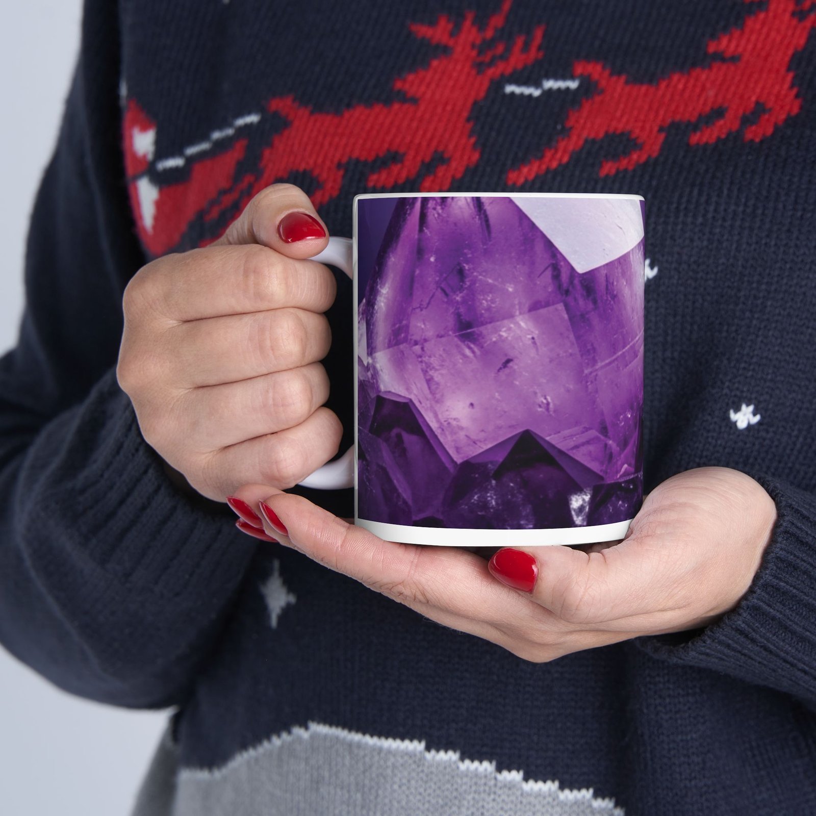 A person holding a white ceramic mug featuring a vivid purple amethyst crystal gemstone print.