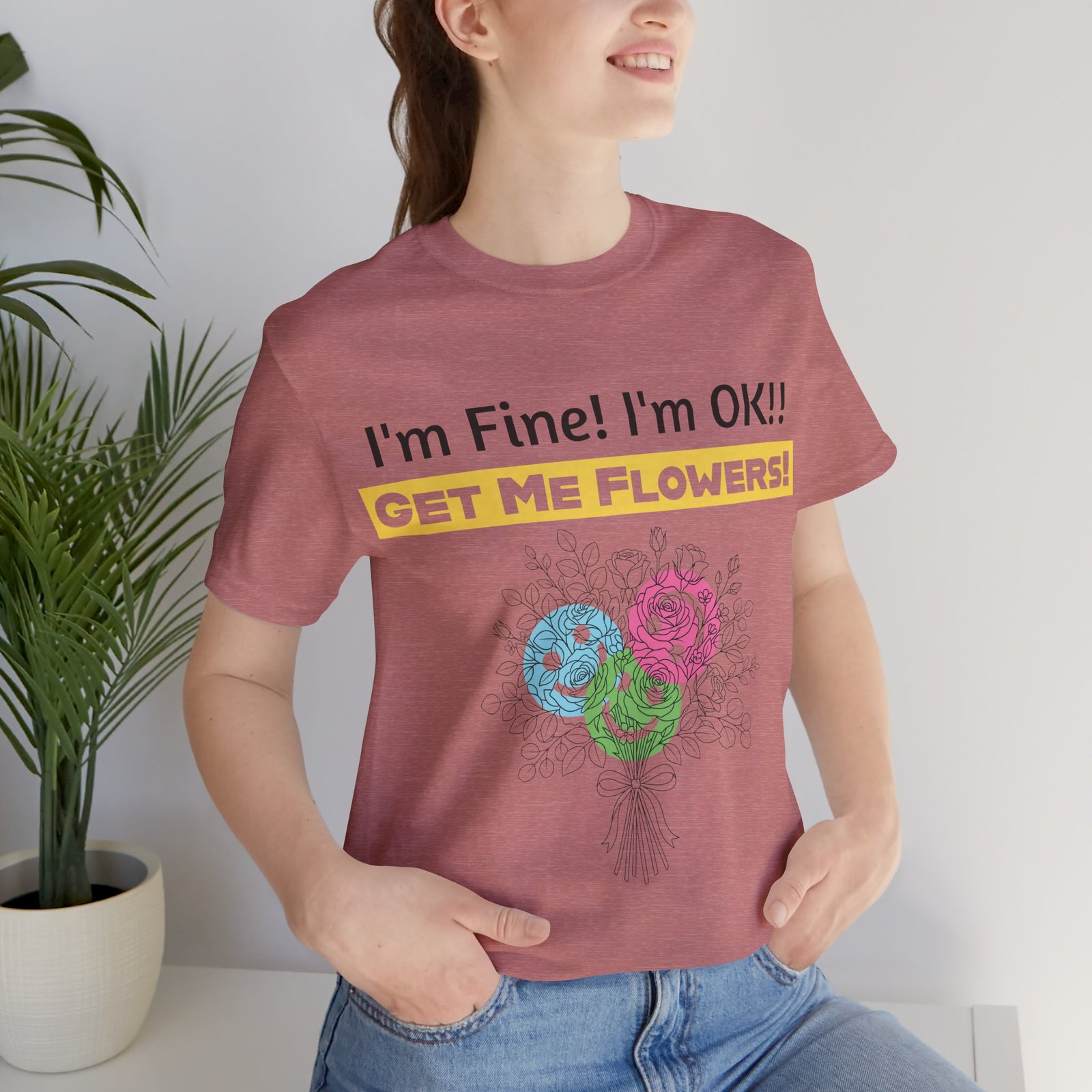 A woman wearing a mauve cotton t-shirt with a colorful floral graphic and the text I'm Fine! I'm OK!! Get Me Flowers!