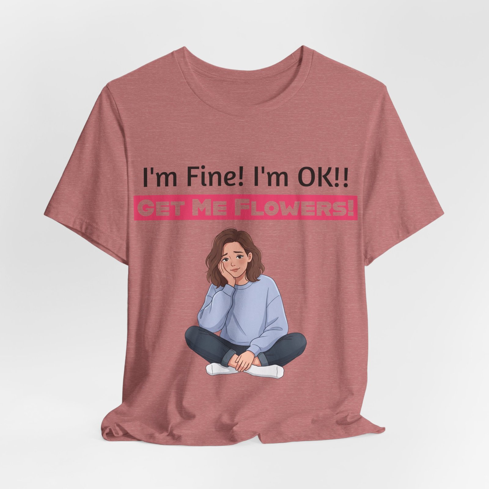 Dusty rose t-shirt featuring a cartoon of a woman sitting with her chin in her hand, above text saying I'm Fine! I'm OK!! GET ME FLOWERS!