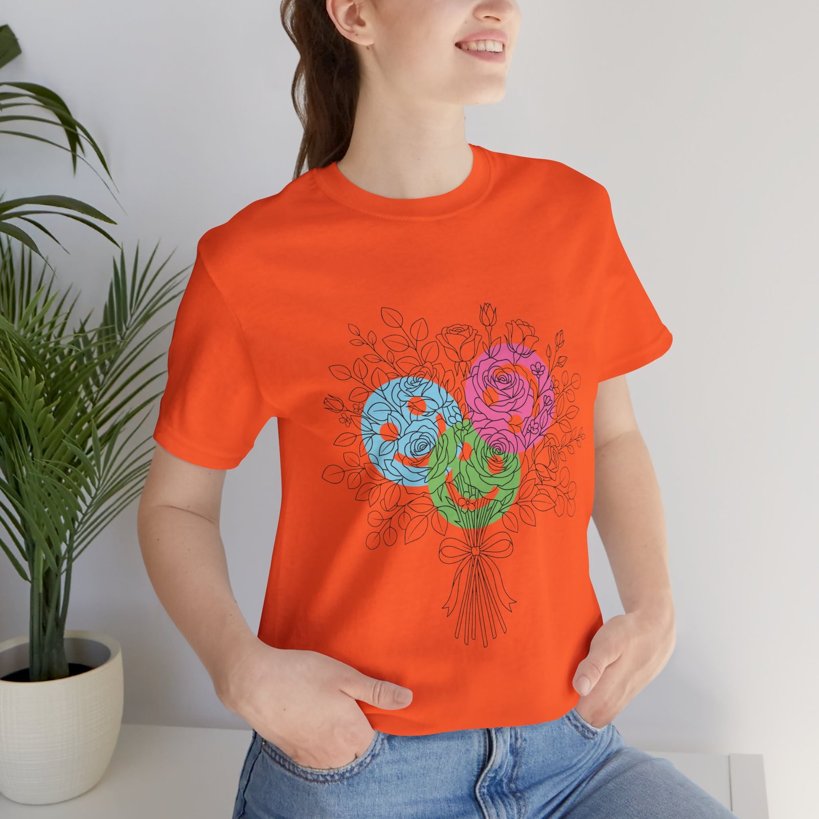 Orange t-shirt featuring a colorful hand-drawn bouquet of teal, magenta, and lime floral yarn blooms.