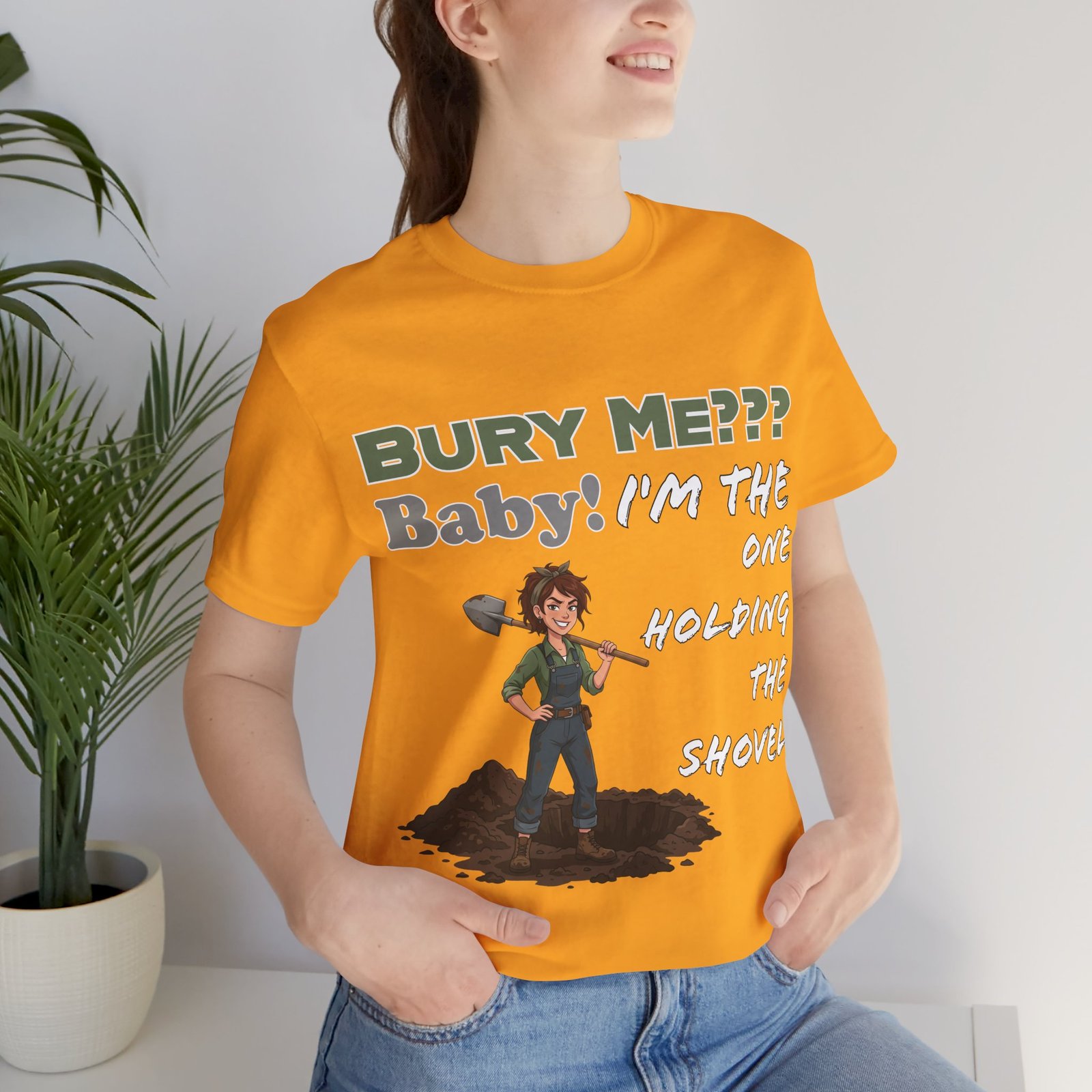 Orange T-shirt featuring an illustrated character holding a shovel and dark humor text "BURY ME??? Baby! I'm the ONE HOLDING THE SHOVEL"