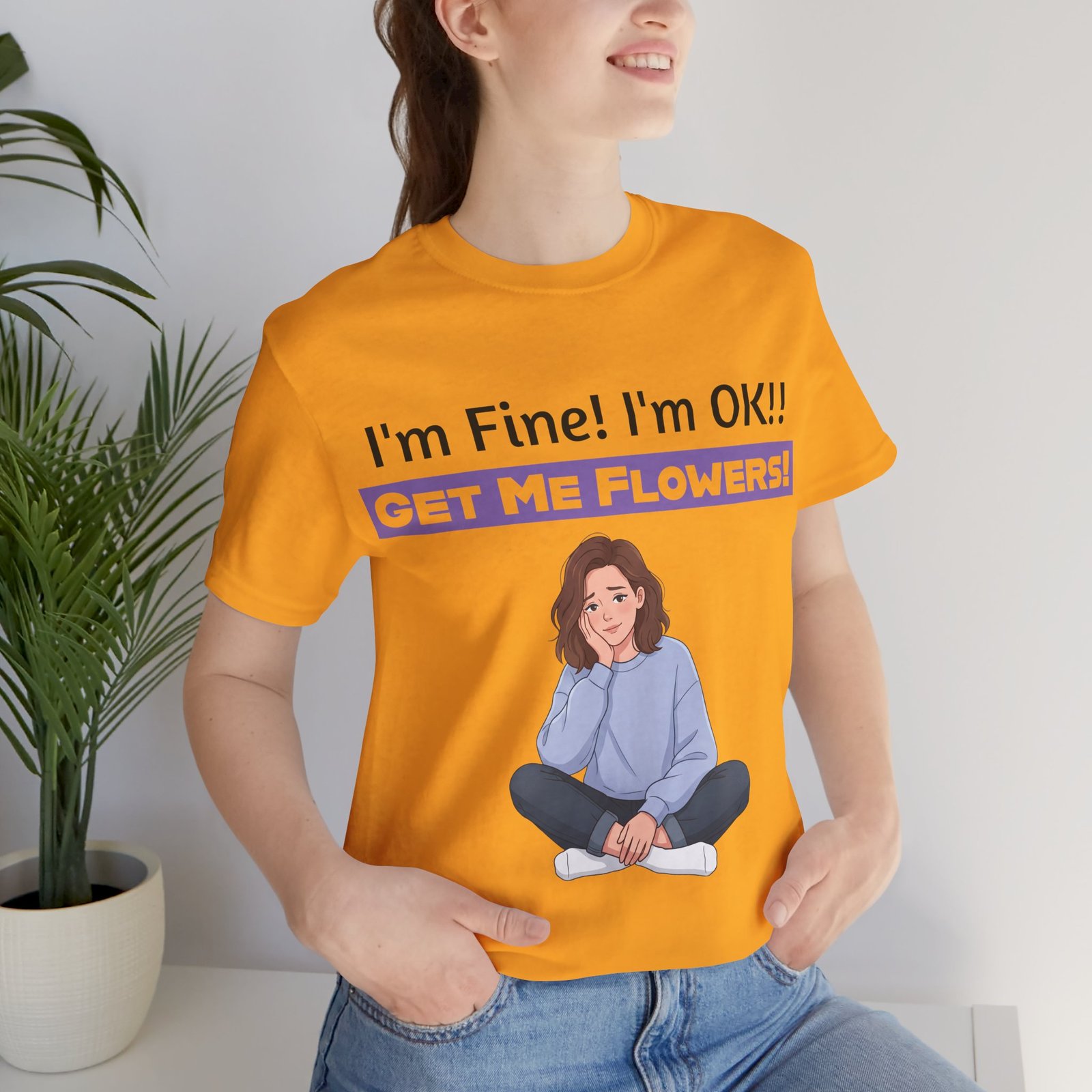 Orange t-shirt featuring an illustration of a seated girl and the text 'I'm Fine! I'm OK!! GET ME FLOWERS!'