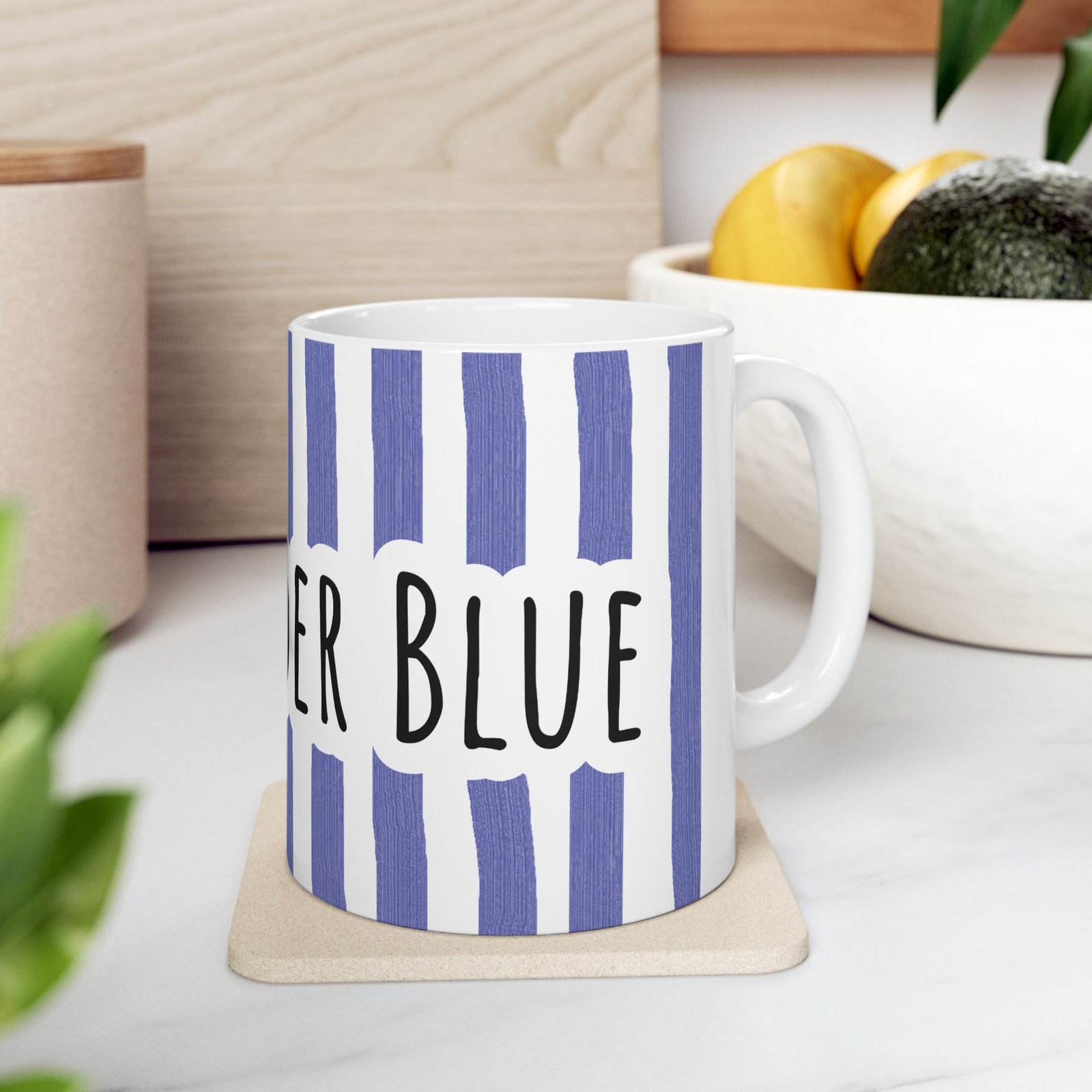 Periwinkle striped ceramic mug with hand-lettered 'Stay Under Blue' text sitting on a beige coaster.