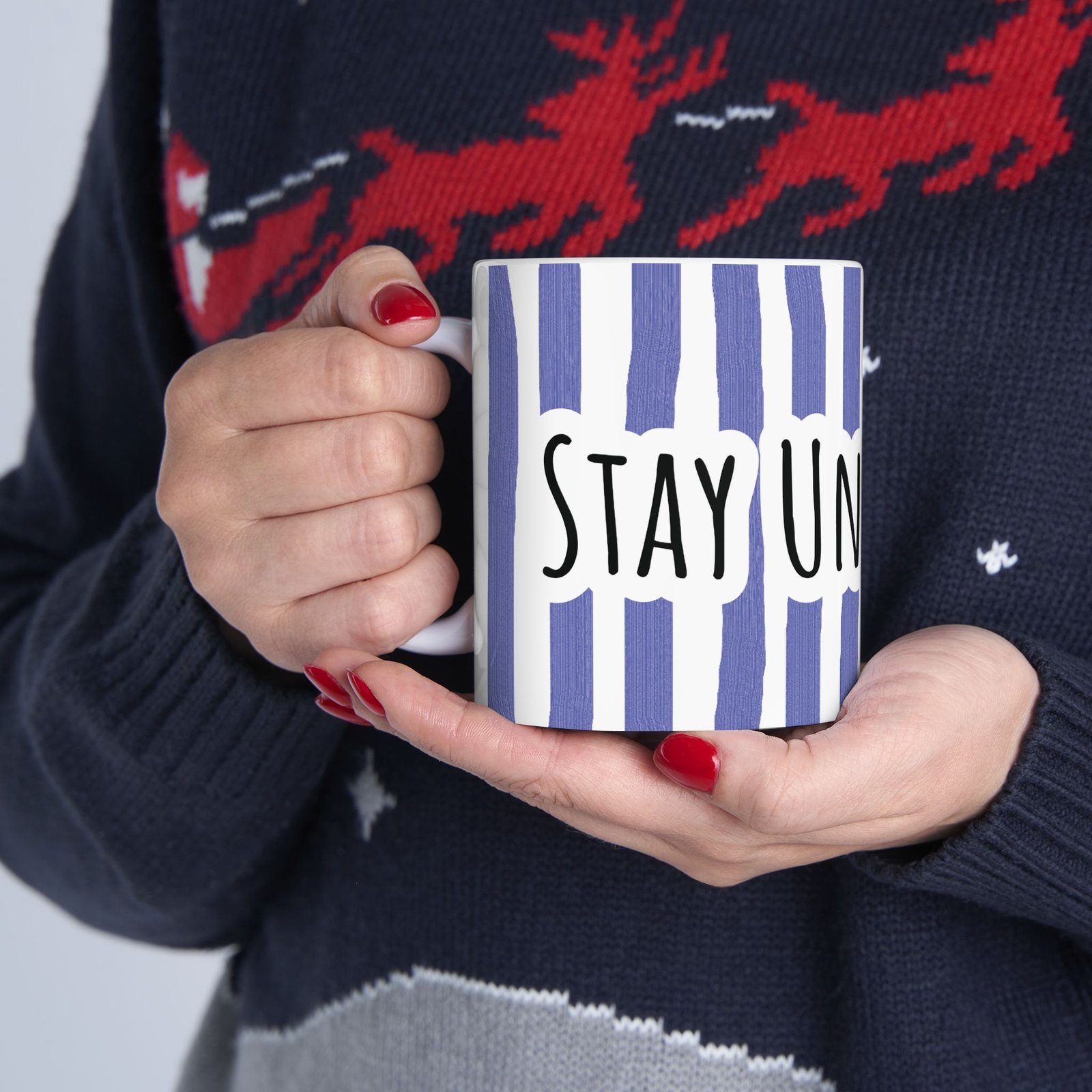 Person holding a white ceramic mug with periwinkle vertical stripes and hand-lettered 'Stay Under Blue' text.