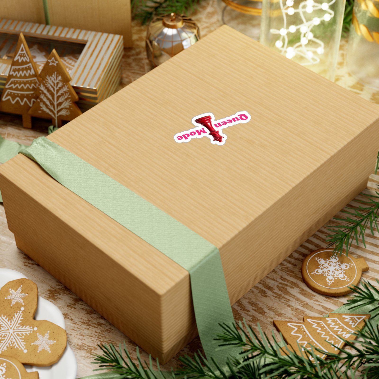 Queen Mode red chess queen sticker on a wooden gift box decorated with green ribbon and holiday gingerbread cookies.