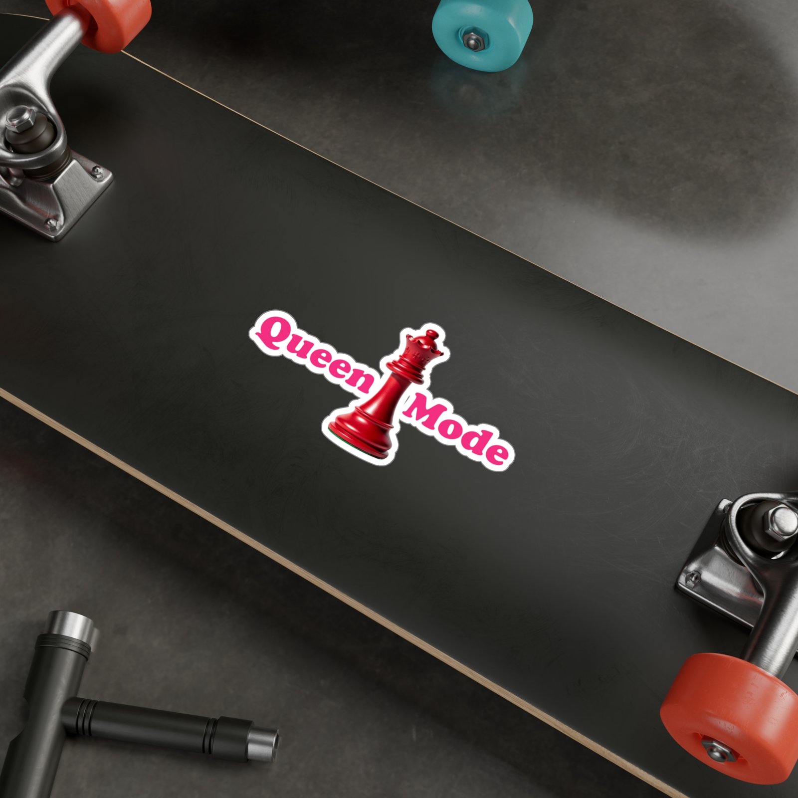 Queen Mode red chess queen sticker with pink text on a black skateboard surface.
