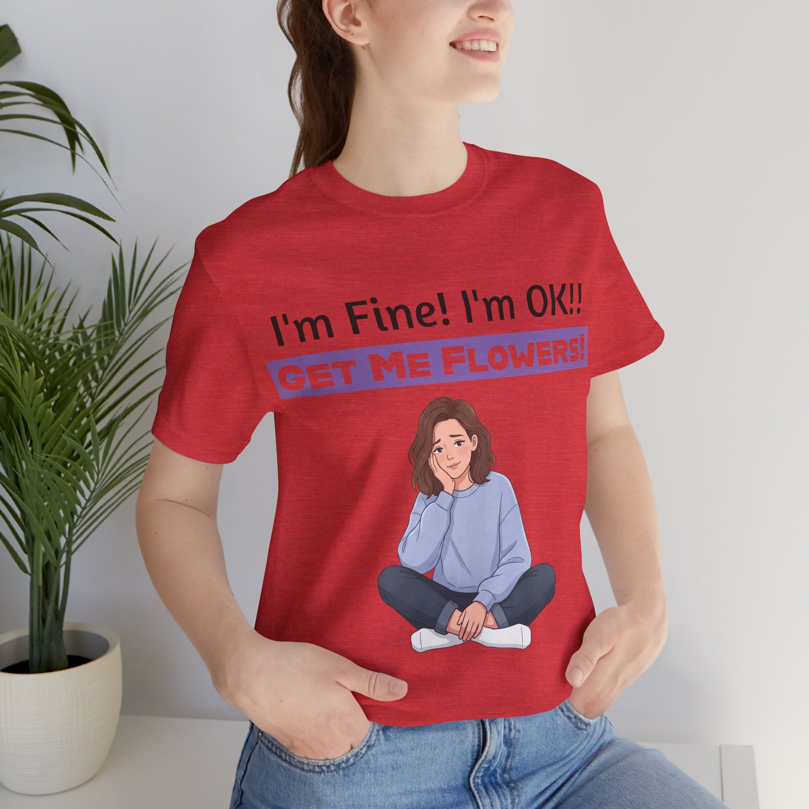 Red t-shirt featuring a cartoon girl sitting and text saying "I'm Fine! I'm OK!! GET ME FLOWERS!"