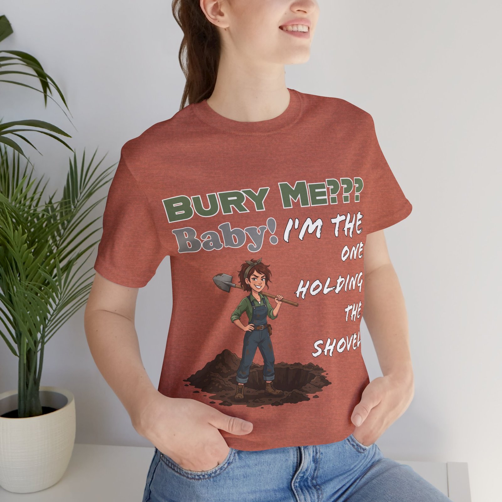 Rust-colored t-shirt featuring a cartoon character holding a shovel and the text 'Bury Me??? Baby! I'm the One Holding the Shovel'.