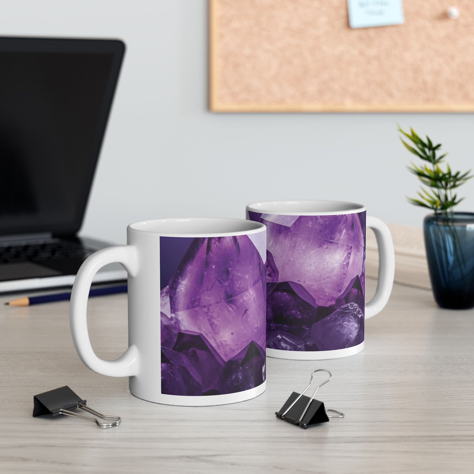 Two white ceramic mugs featuring a vivid purple amethyst crystal pattern sitting on a light desk with office accessories.
