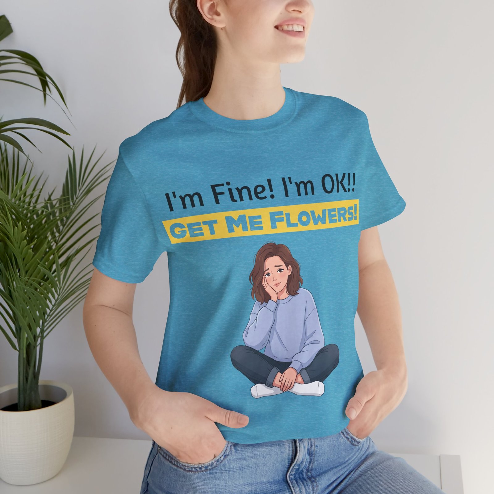 Woman wearing a blue funny t-shirt with 'I'm Fine! I'm OK!! Get Me Flowers!' text and a cartoon girl illustration.