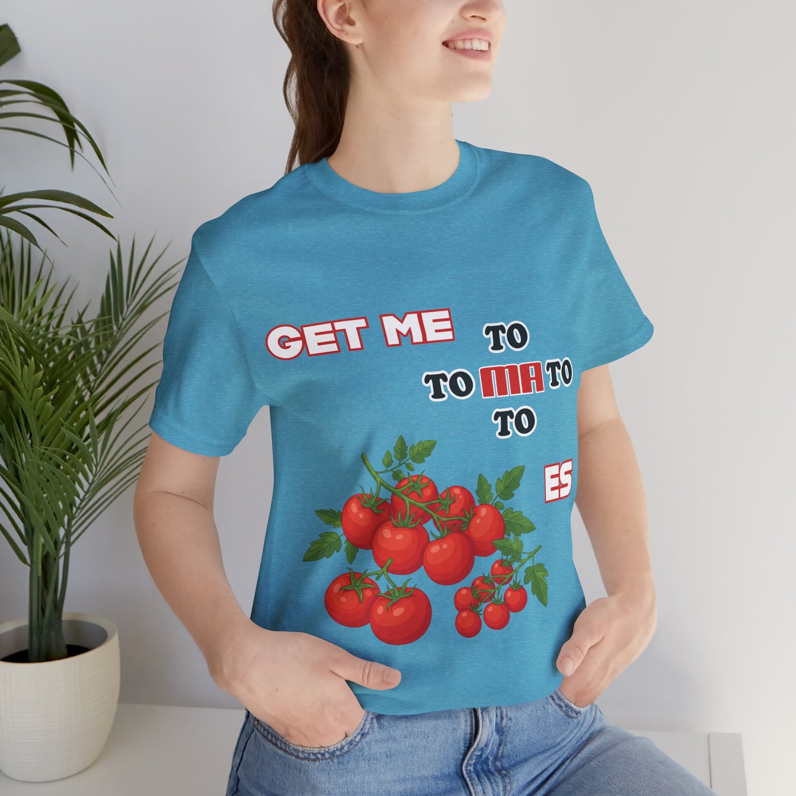 Woman wearing a blue Get Me To Ma To Toes T-Shirt featuring bright red tomato illustrations and bold retro text.