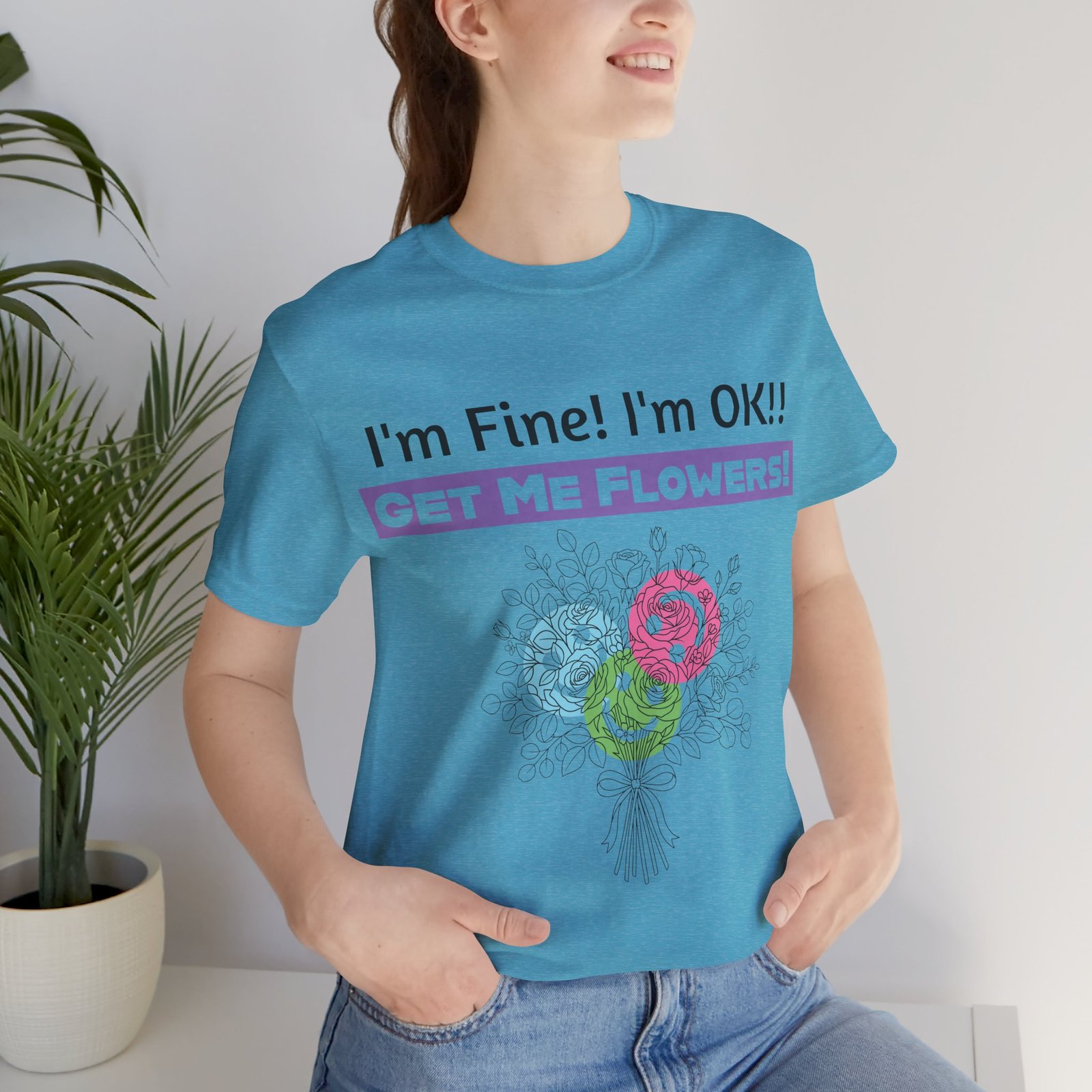 Woman wearing a blue graphic t-shirt with the sarcastic text "I'm Fine! I'm OK!! GET ME FLOWERS!" and a floral print.