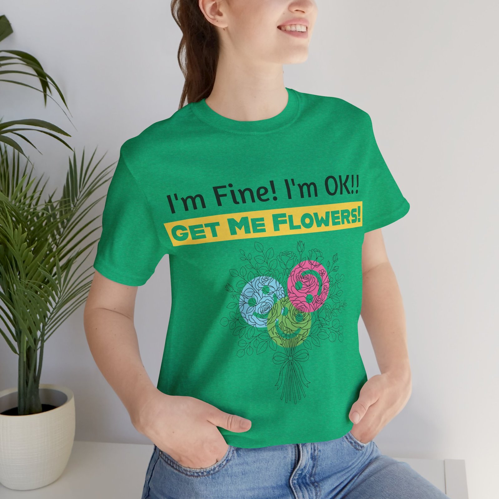Woman wearing a green crew-neck t-shirt with a colorful flower bouquet and the text I'm Fine! I'm OK!! GET ME FLOWERS!