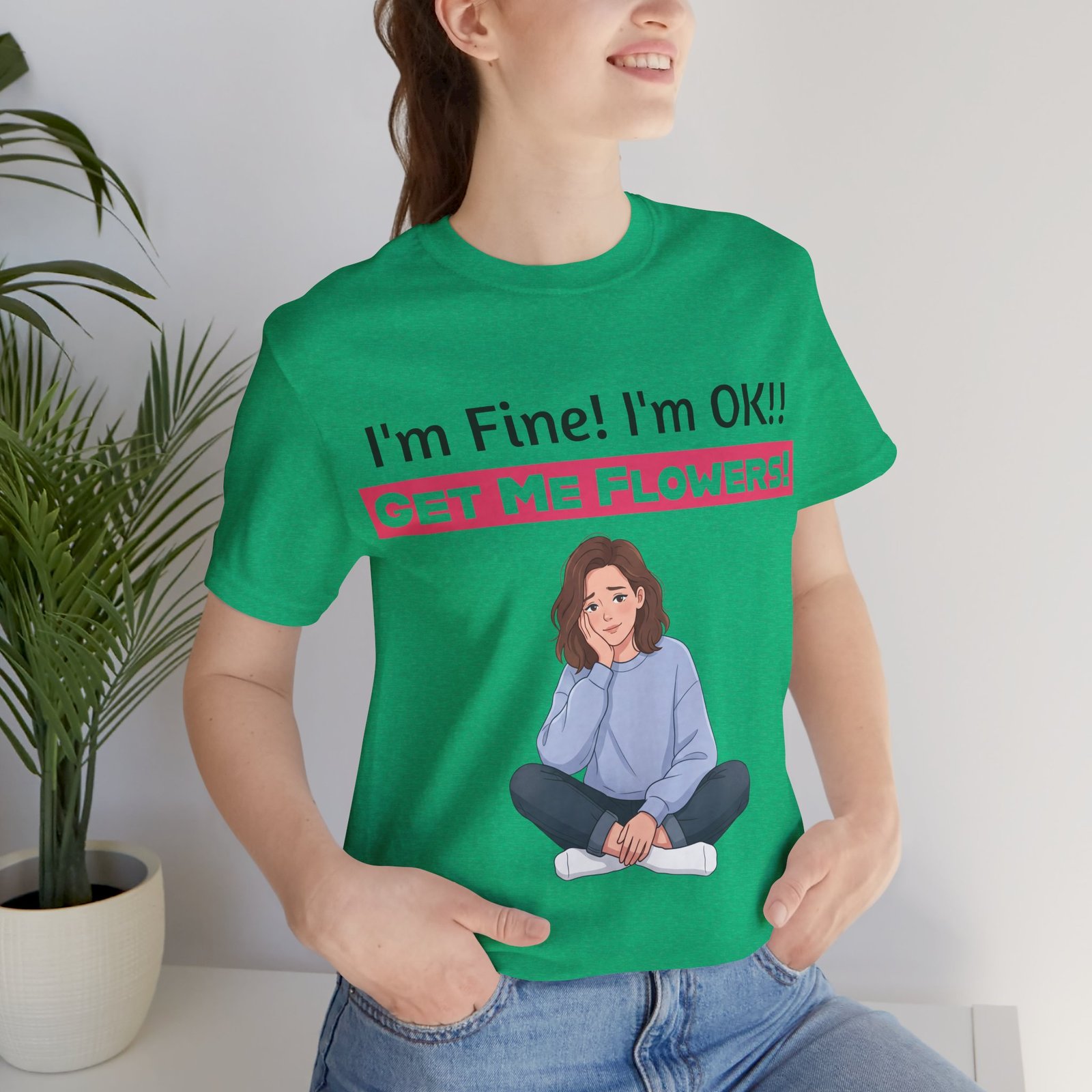 Woman wearing a green funny t-shirt that says I'm Fine! I'm OK!! Get Me Flowers! with a cartoon graphic.