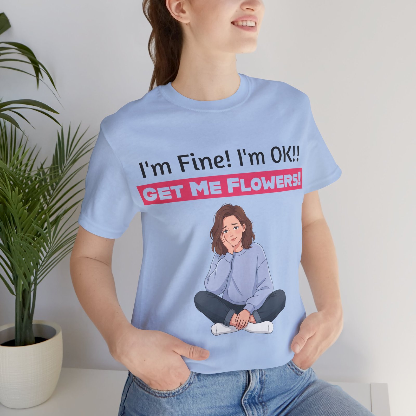 Woman wearing a light blue funny T-shirt with 'I'm Fine! I'm OK!! GET ME FLOWERS!' and a cartoon graphic.