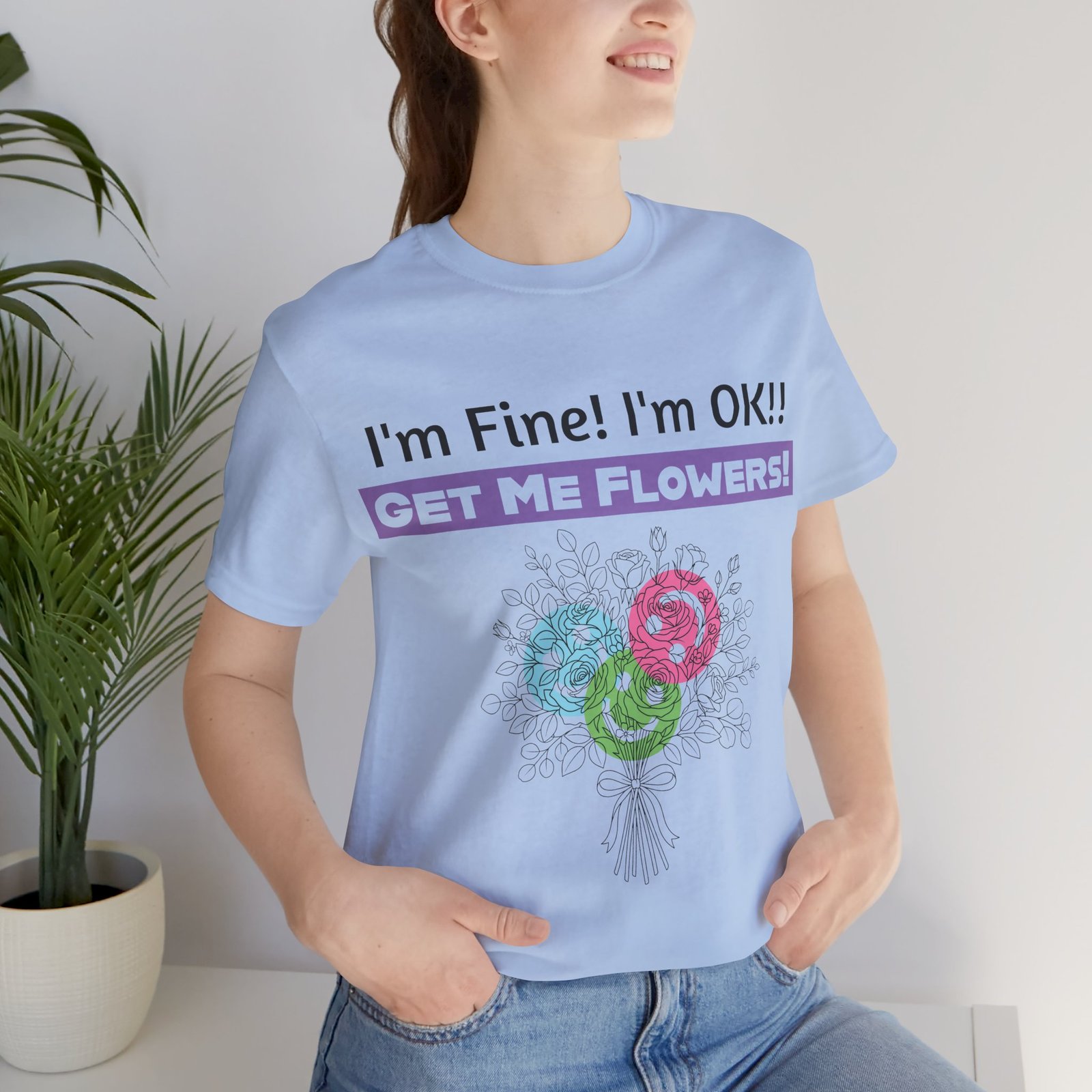 Woman wearing a light blue graphic t-shirt with "I'm Fine! I'm OK!! GET ME FLOWERS!" text and colorful floral sketch.