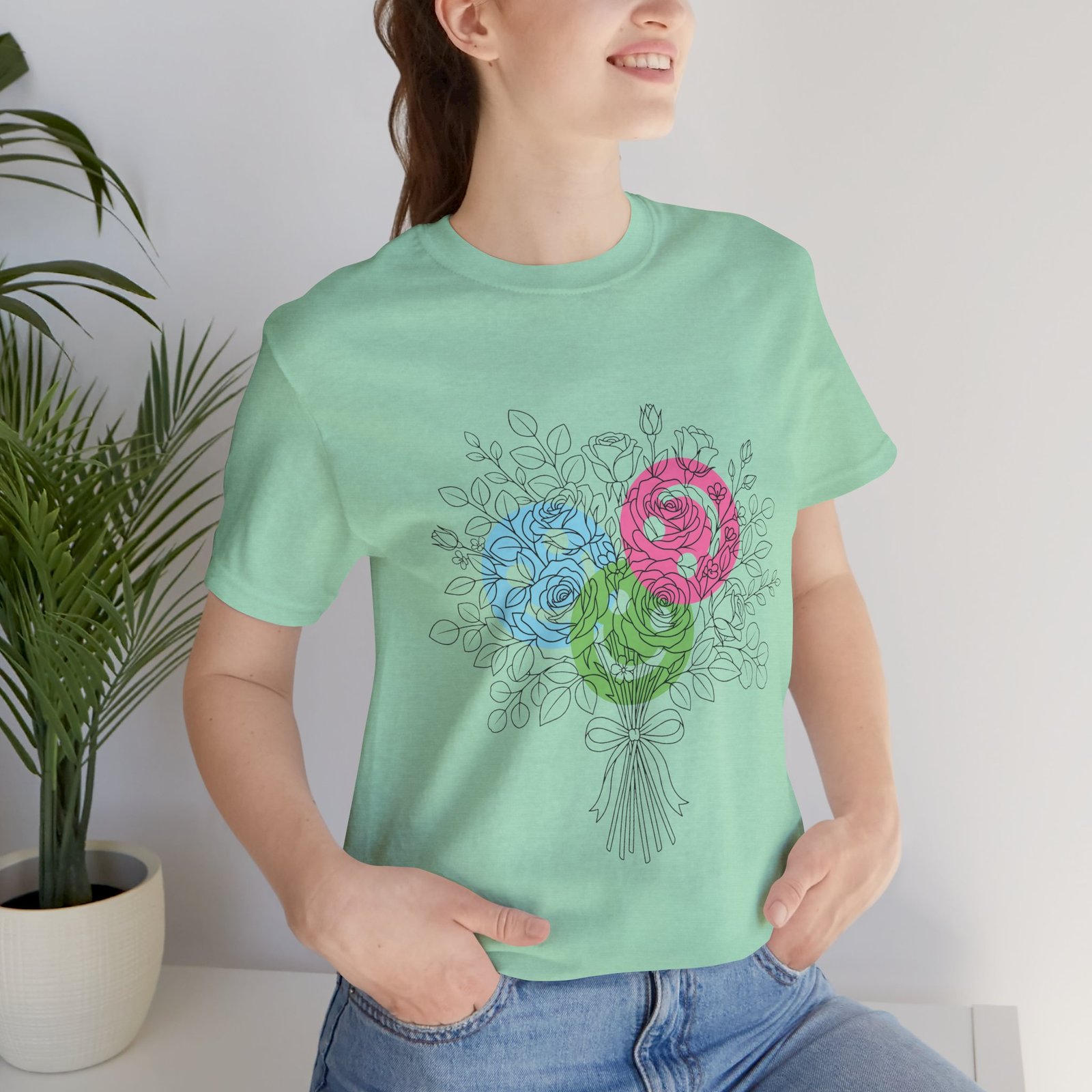 Woman wearing a mint green t-shirt featuring a hand-drawn bouquet of teal, magenta, and lime floral yarn designs.