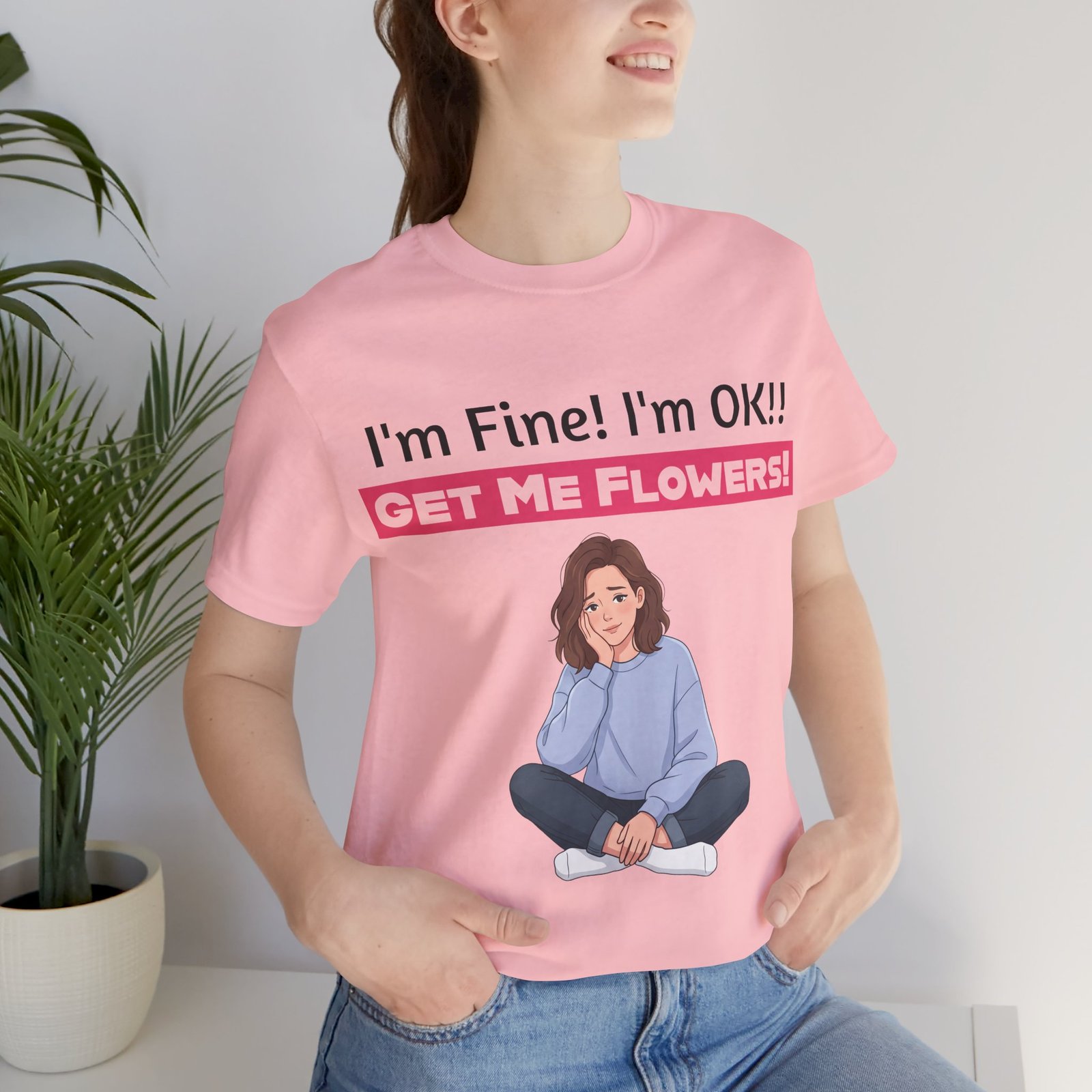 Woman wearing a pink 'I'm Fine! I'm OK!! Get Me Flowers!' funny t-shirt with a cartoon graphic of a seated girl.