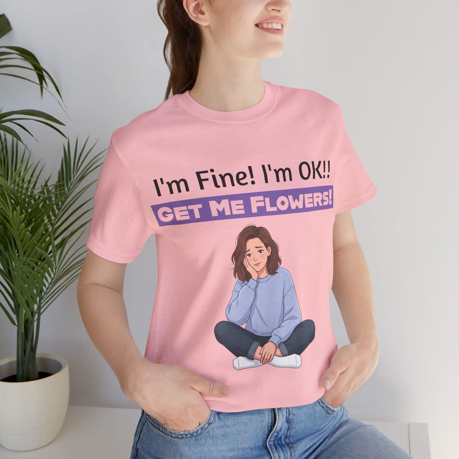 Woman wearing a pink t-shirt with I'm Fine! I'm OK!! Get Me Flowers! funny graphic and a seated girl illustration.