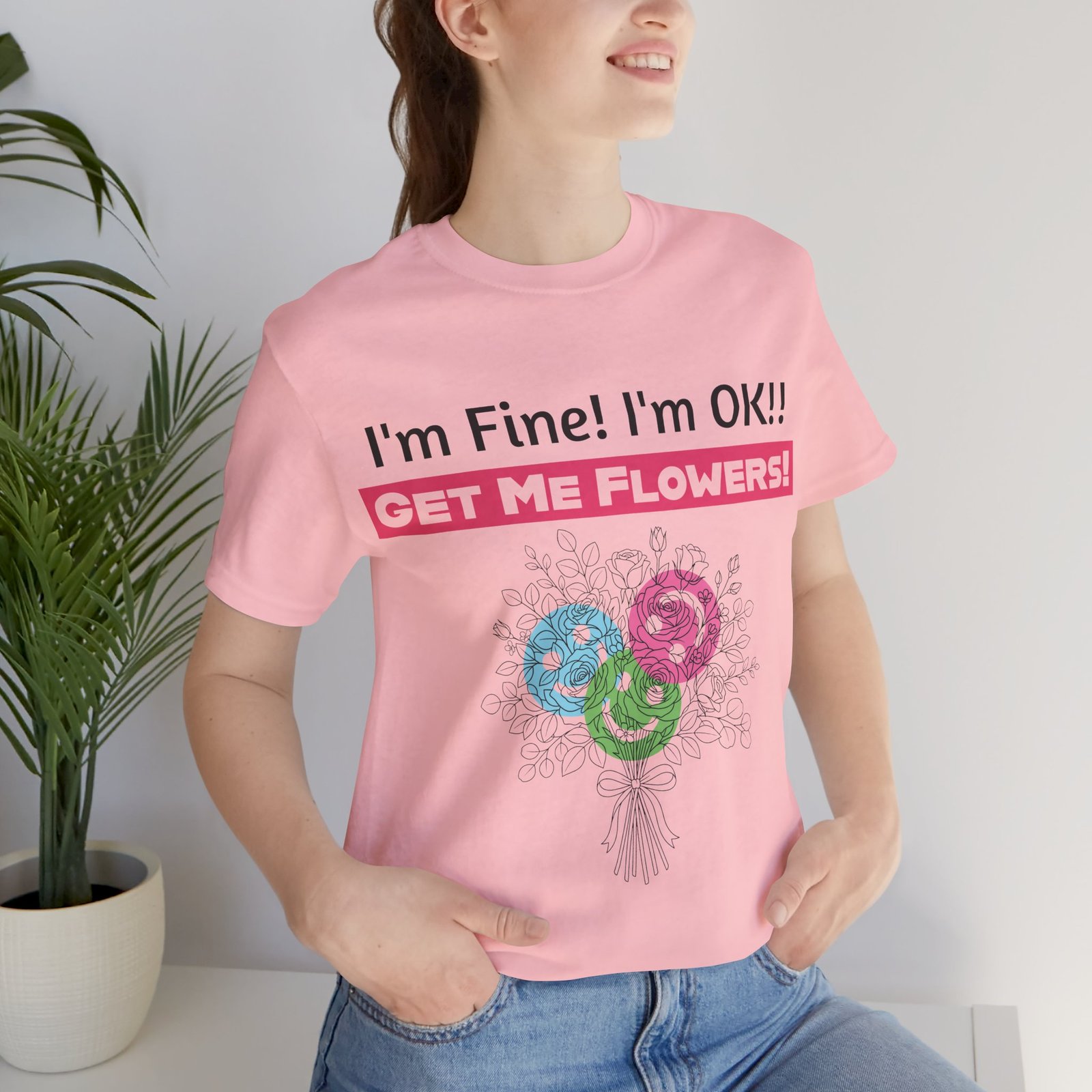 Woman wearing a pink T-shirt with "I'm Fine! I'm OK!! GET ME FLOWERS!" text and a colorful floral bouquet design.