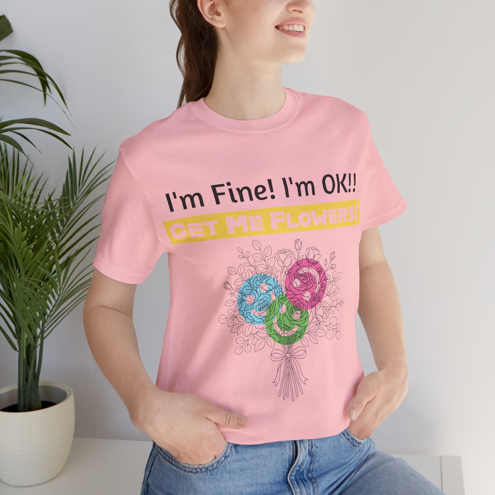Woman wearing a pink t-shirt with "I'm Fine! I'm OK!! GET ME FLOWERS!" text and a colorful flower bouquet graphic.