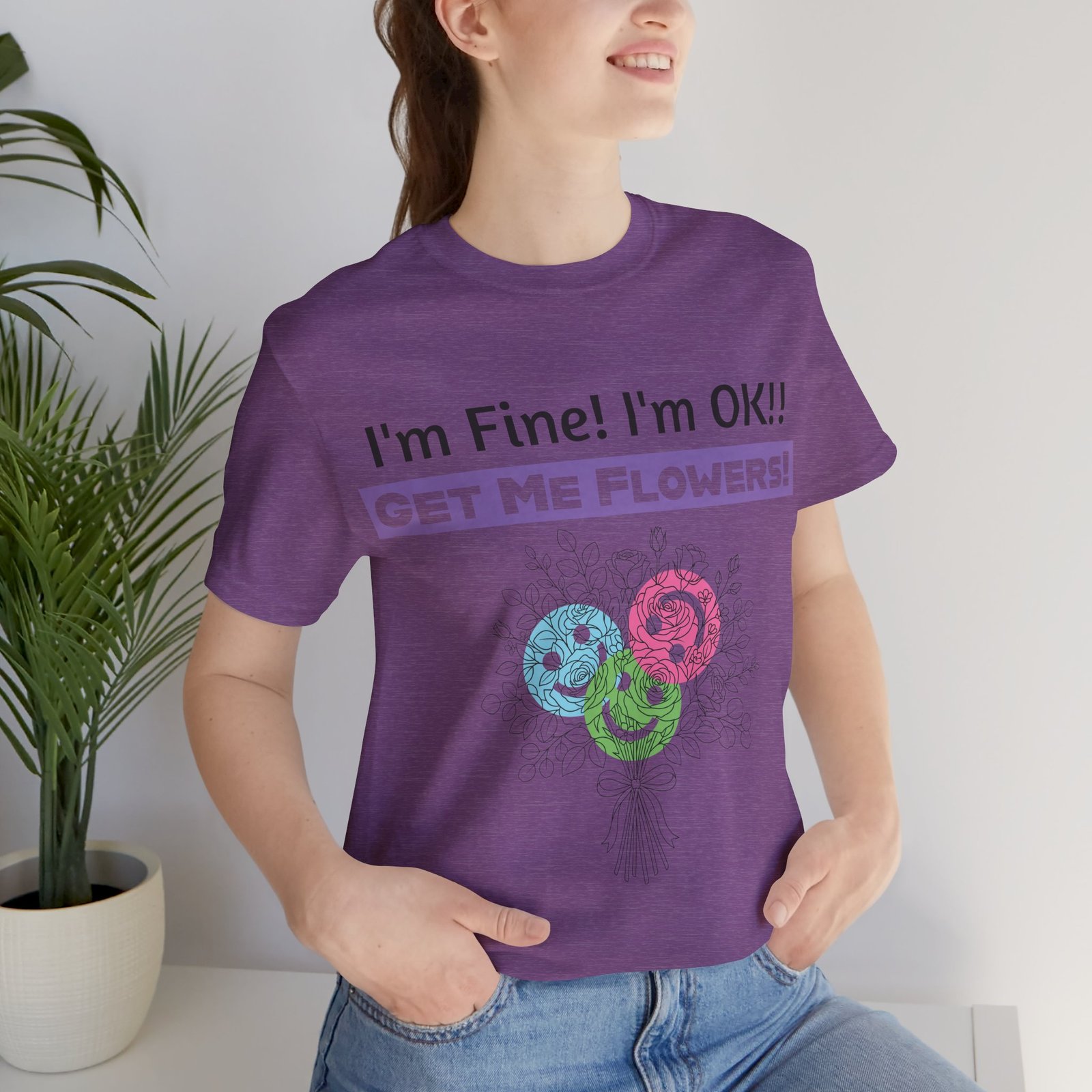 Woman wearing a purple graphic t-shirt with 'I'm Fine! I'm OK!! GET ME FLOWERS!' text and colorful floral bouquet print.