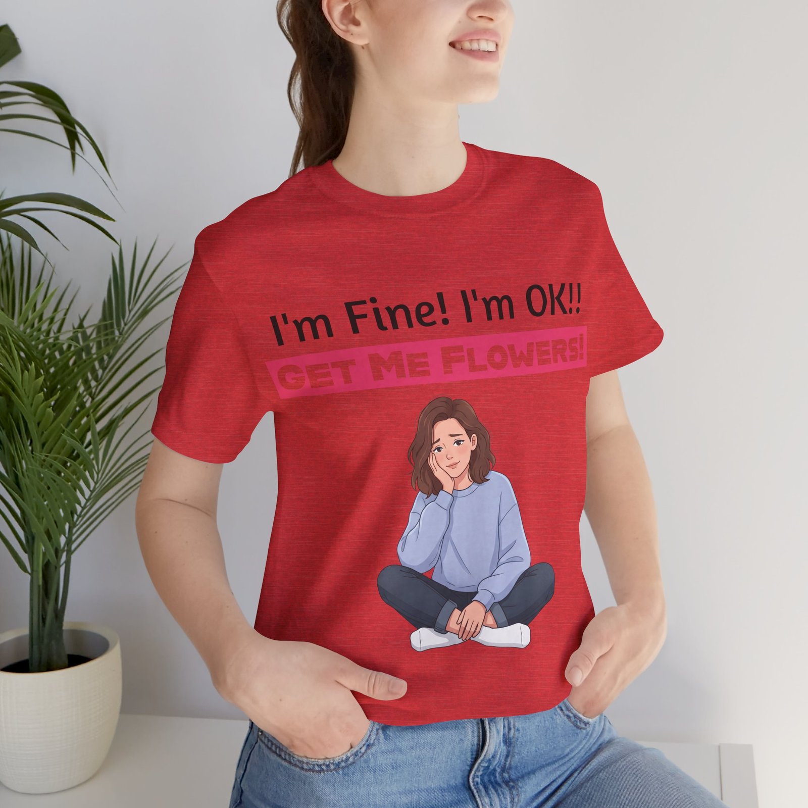 Woman wearing a red funny t-shirt featuring an illustration of a seated person and text: I'm Fine! I'm OK!! GET ME FLOWERS!