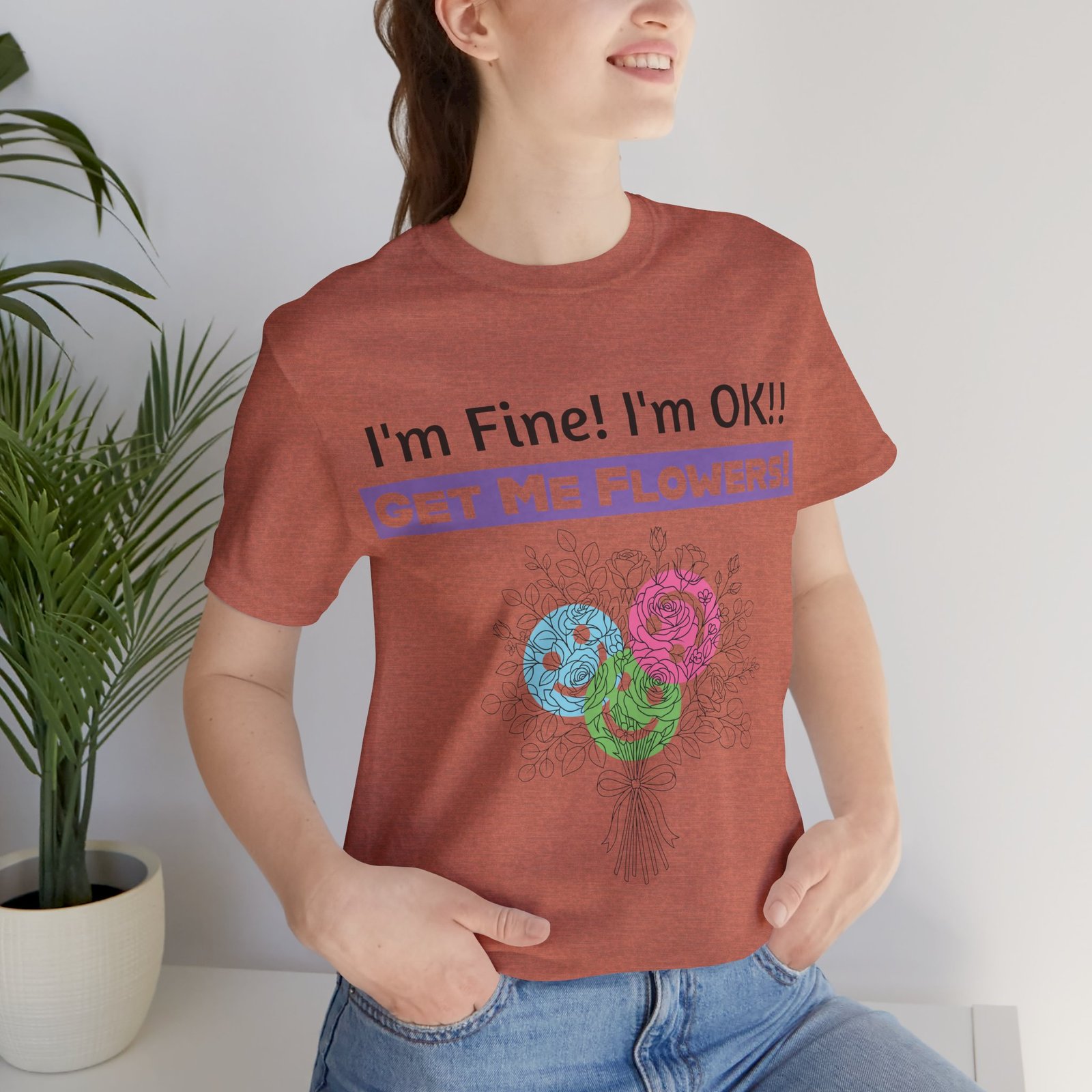 Woman wearing a rust-colored graphic t-shirt with "I'm Fine! I'm OK!! GET ME FLOWERS!" text and colorful floral art.