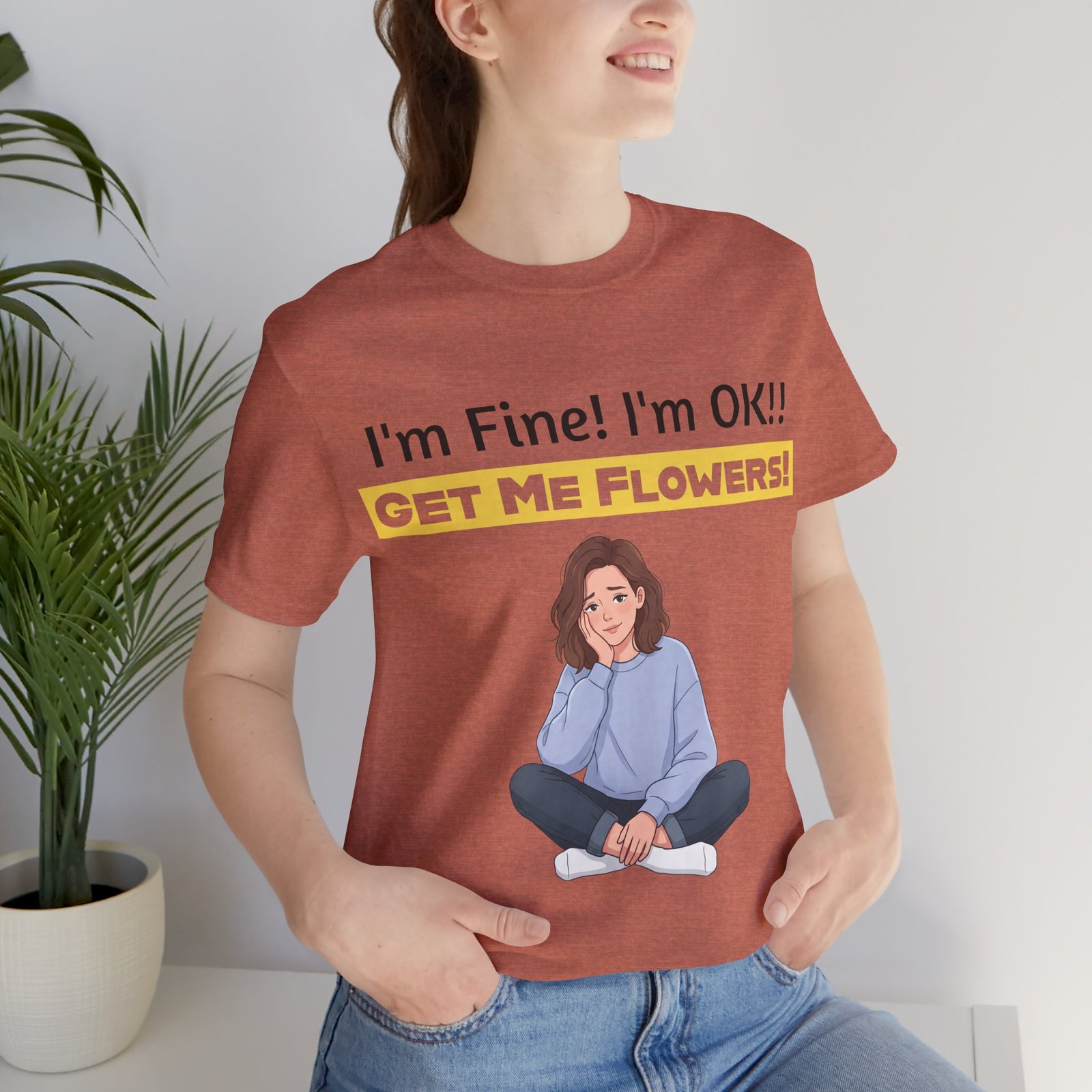 Woman wearing a rust-colored I'm Fine! I'm OK!! Get Me Flowers! Funny T-Shirt with a cartoon illustration of a seated girl.