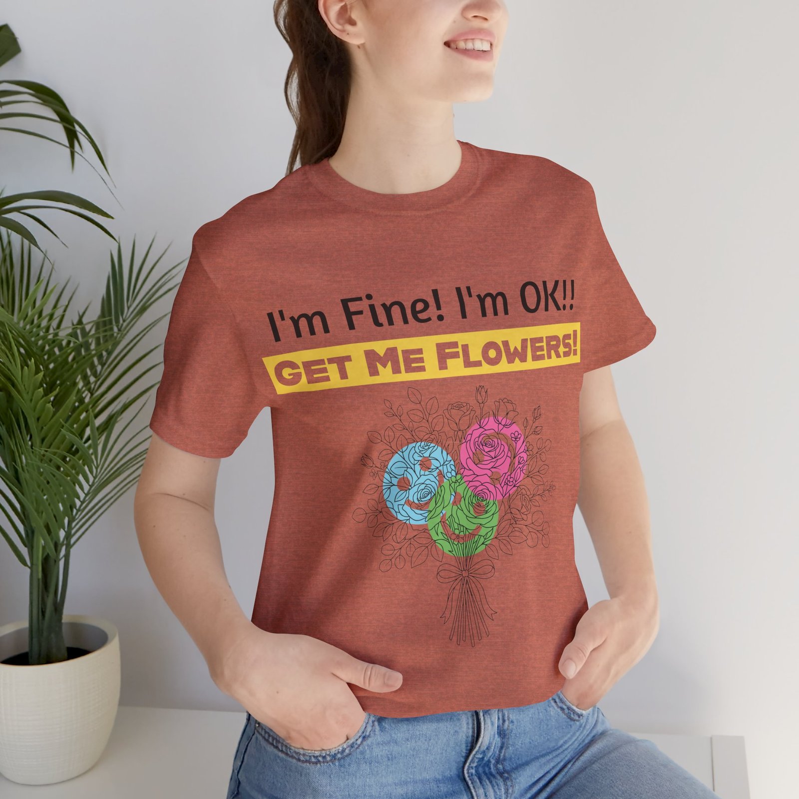 Woman wearing a terracotta crew-neck t-shirt featuring a colorful abstract flower bouquet and "I'm Fine! I'm OK!! GET ME FLOWERS!" text.