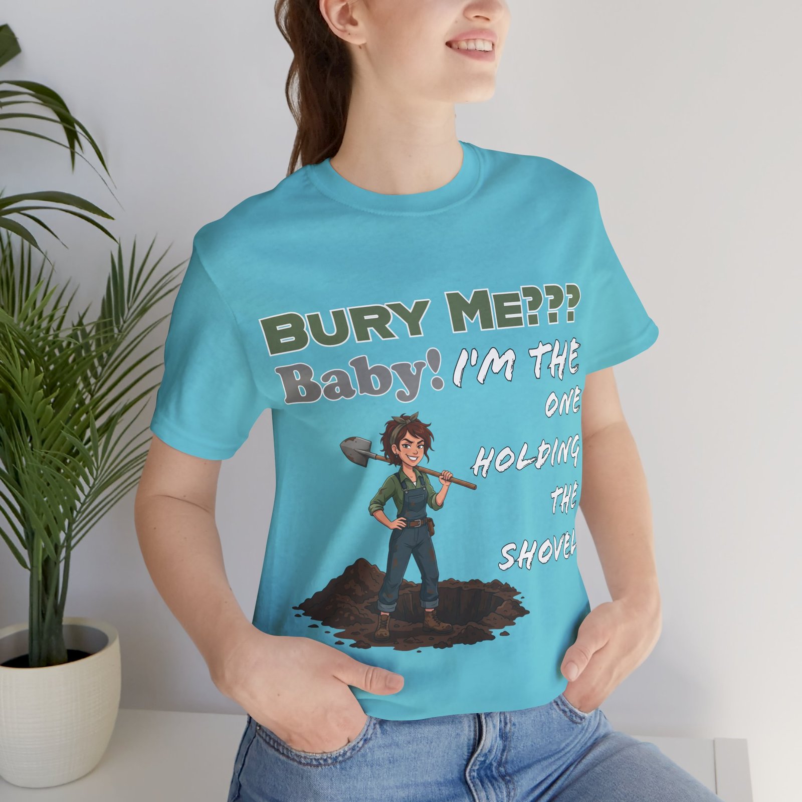 Woman wearing a turquoise t-shirt with a cartoon character holding a shovel and the text "Bury Me??? Baby! I'm the One Holding the Shovel".