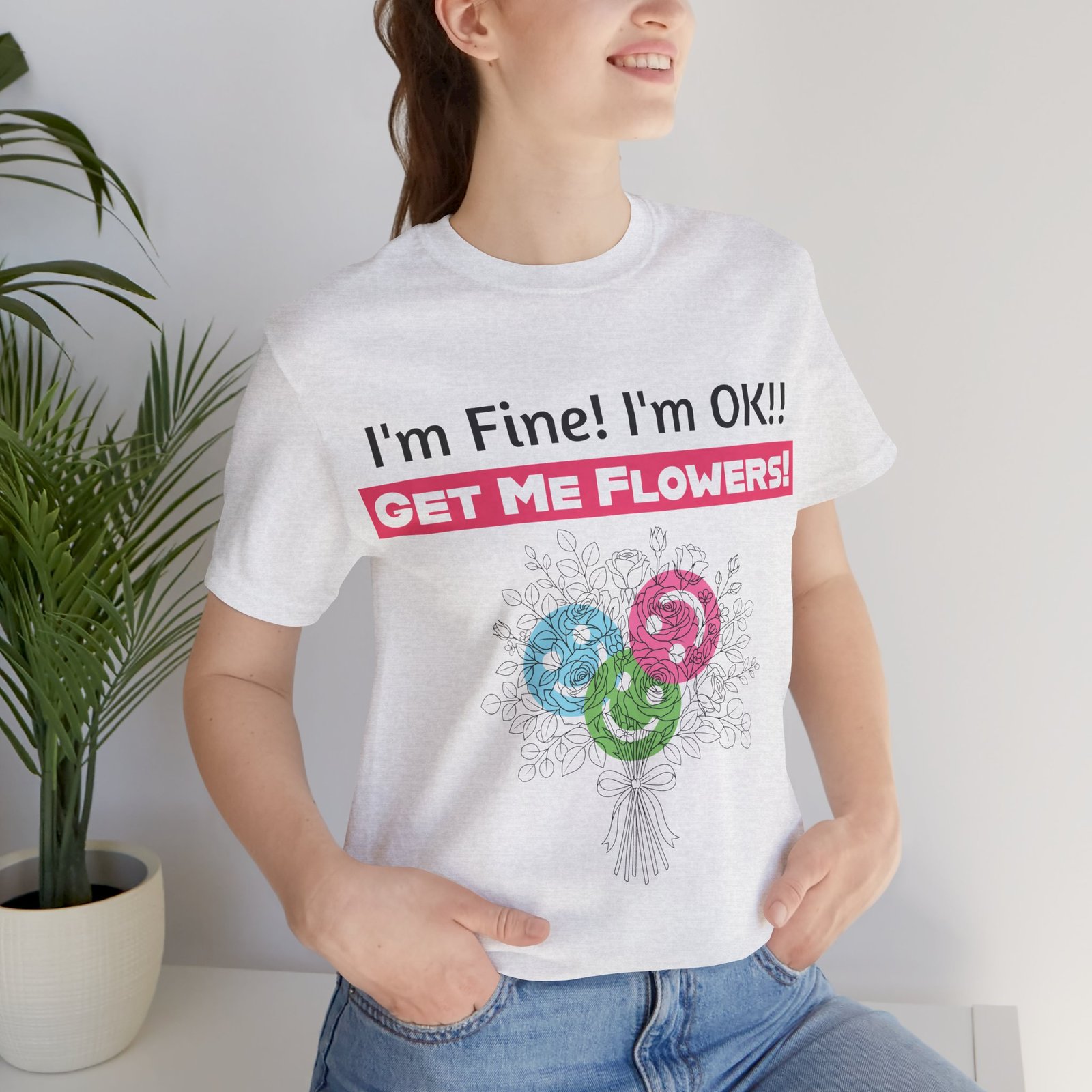 Woman wearing a white crew-neck T-shirt with "I'm Fine! I'm OK!! GET ME FLOWERS!" text and a colorful floral graphic.