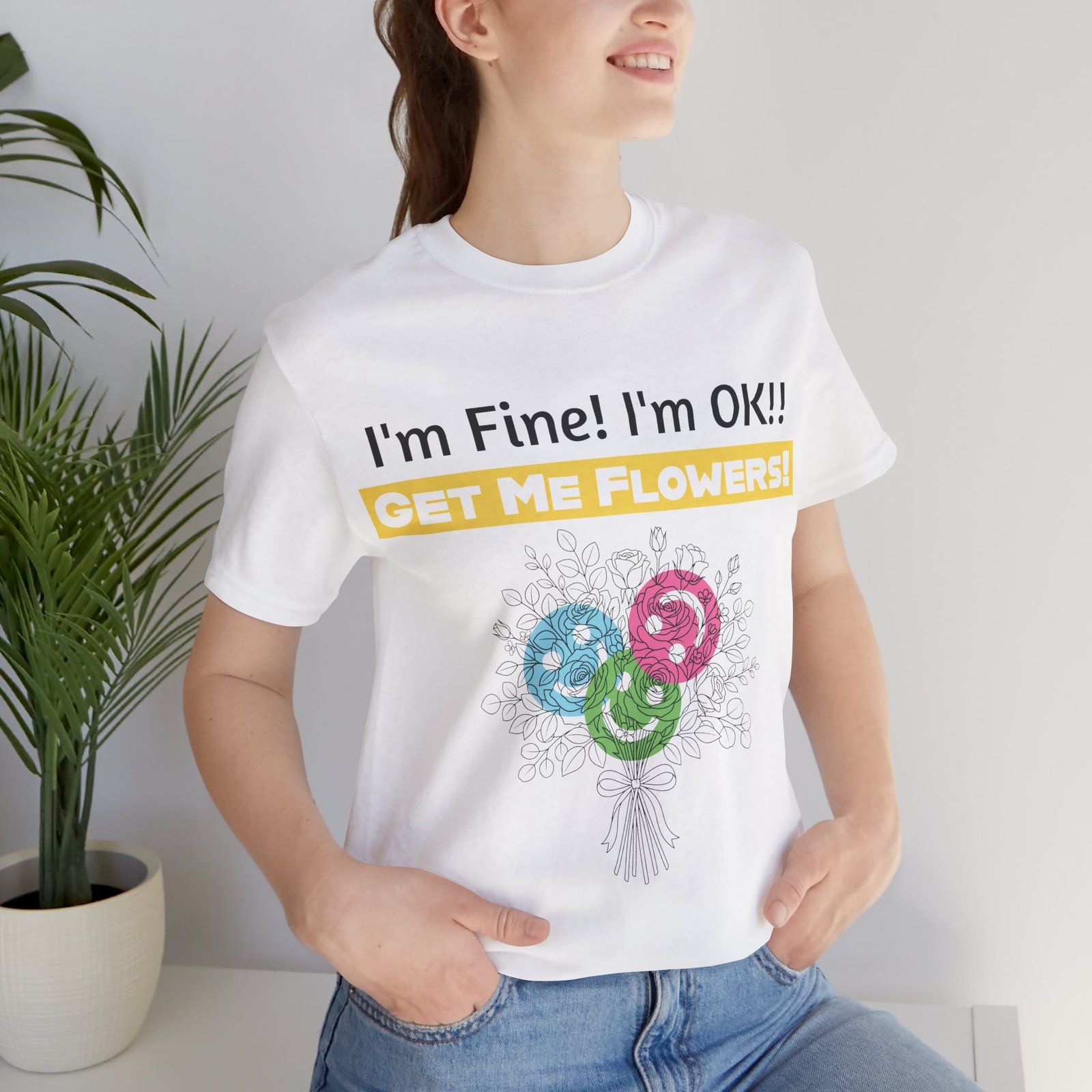 Woman wearing a white crew-neck t-shirt with the text "I'm Fine! I'm OK!! GET ME FLOWERS!" and colorful flower graphic.