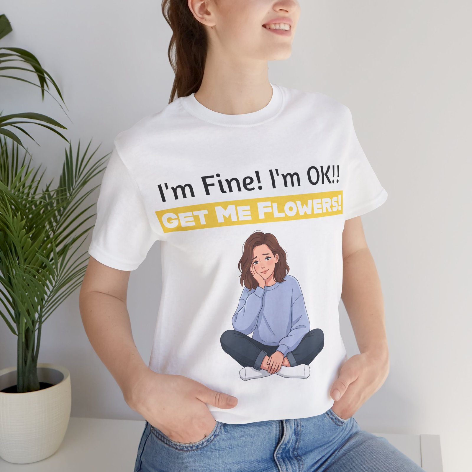 Woman wearing a white crewneck t-shirt with "I'm Fine! I'm OK!! GET ME FLOWERS!" text and a cartoon girl illustration.