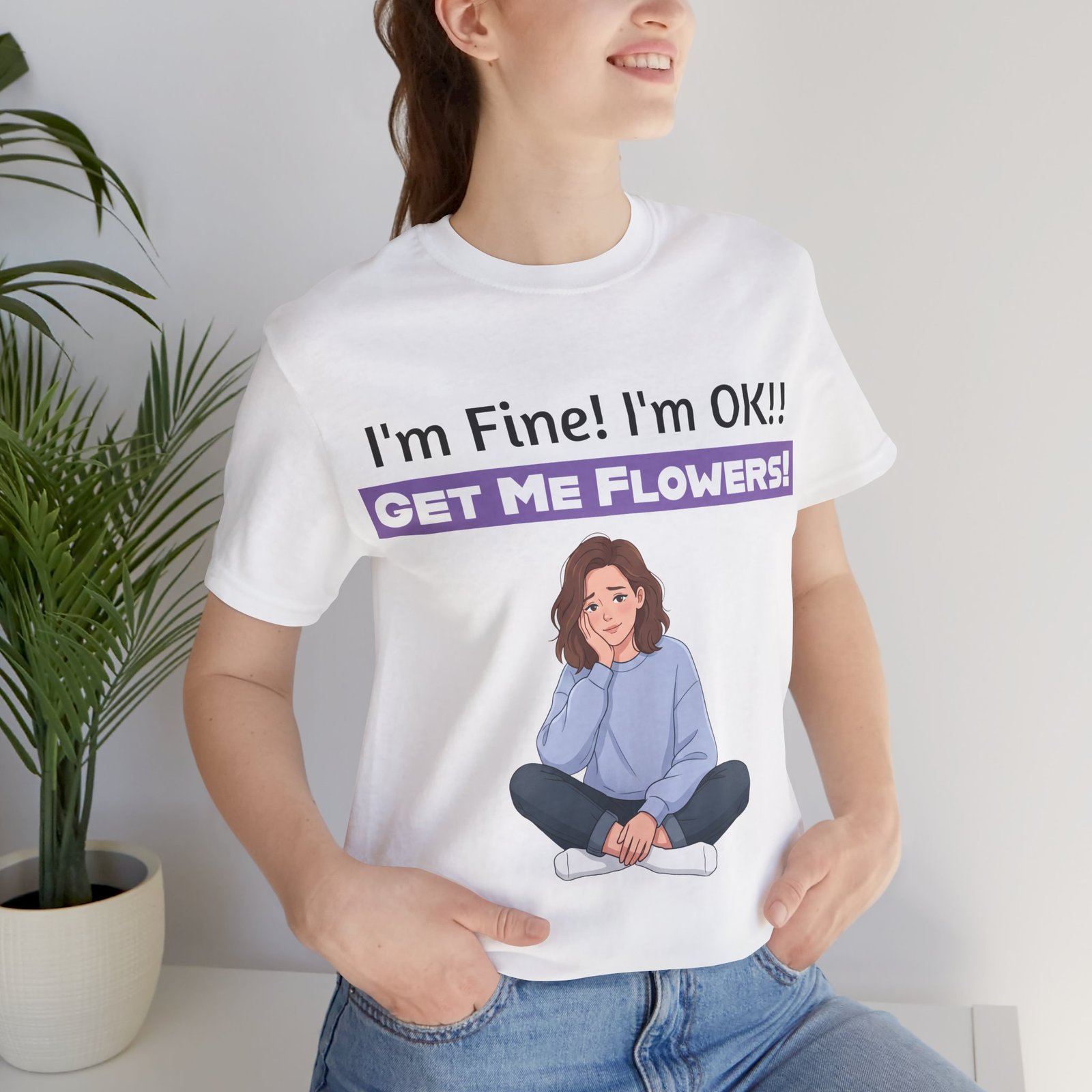 Woman wearing a white funny t-shirt with a cartoon girl and text reading I'm Fine! I'm OK!! GET ME FLOWERS!