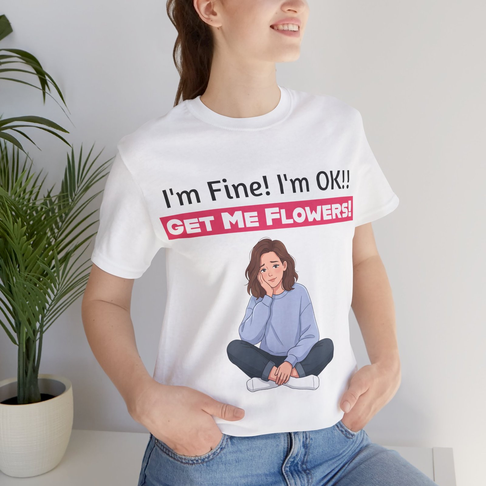 Woman wearing a white funny t-shirt with 'I'm Fine! I'm OK!! GET ME FLOWERS!' text and a cartoon girl illustration.
