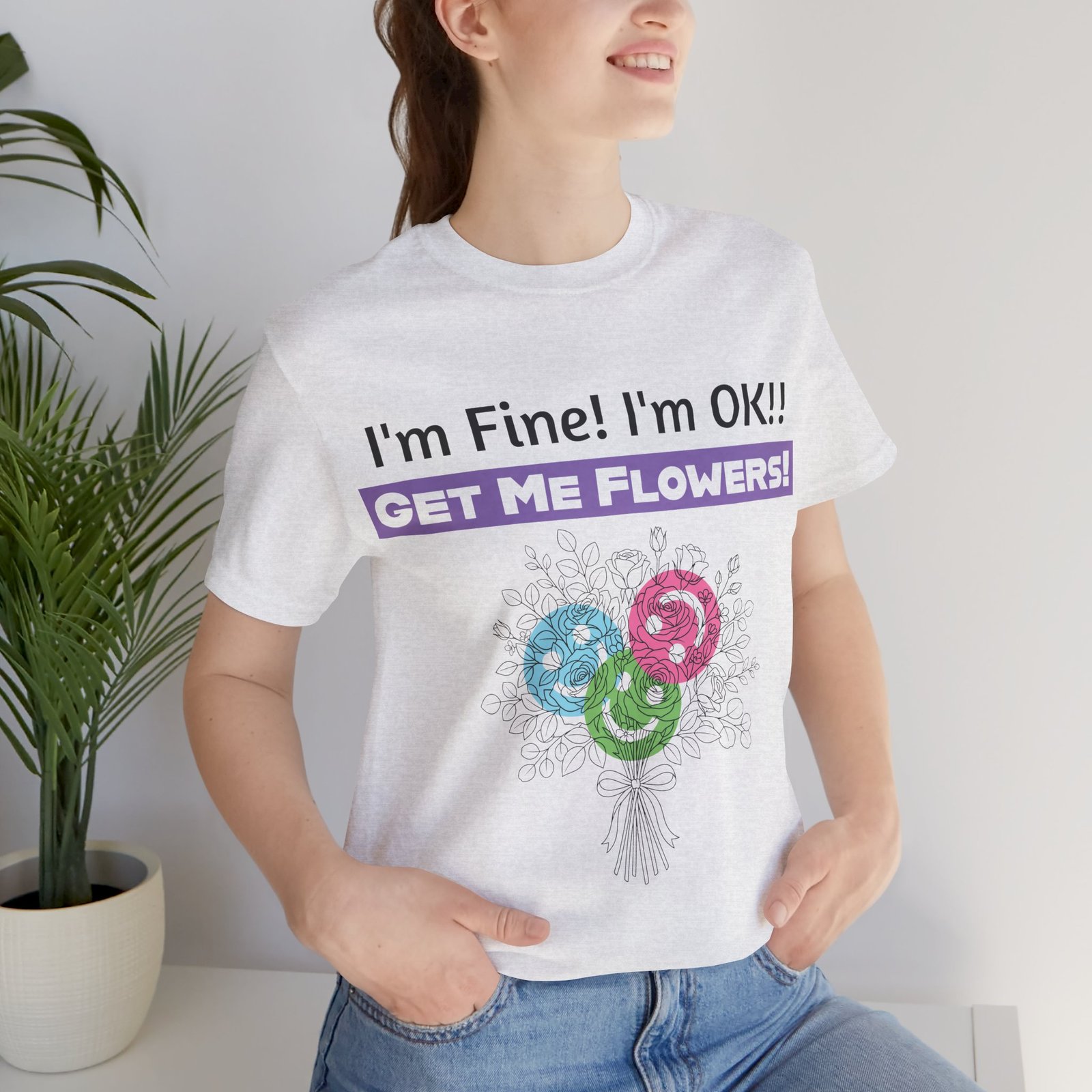 Woman wearing a white graphic t-shirt with 'I'm Fine! I'm OK!! GET ME FLOWERS!' text and a colorful floral bouquet print.
