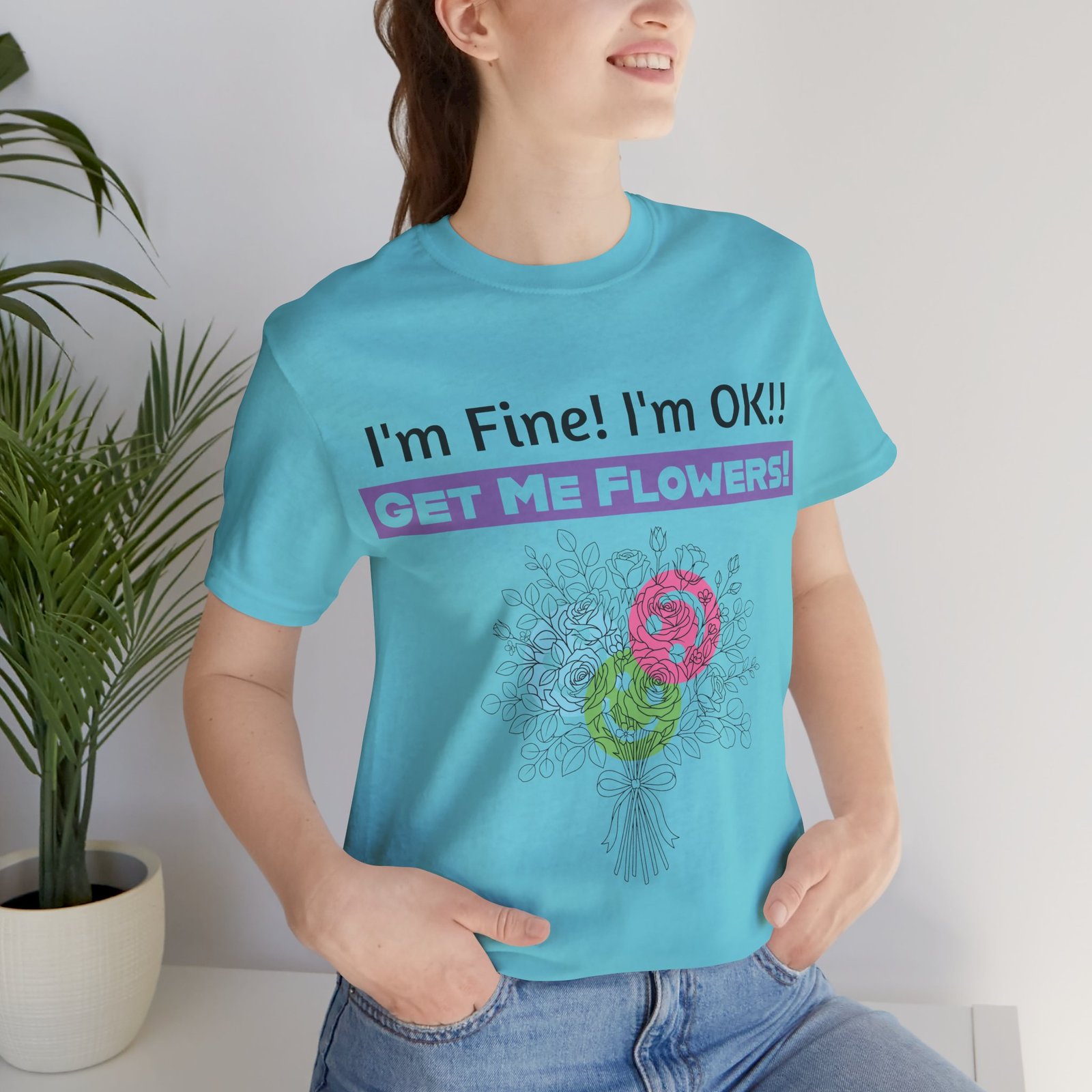 Woman wearing light blue t-shirt with 'I'm Fine! I'm OK!! GET ME FLOWERS!' text and floral graphic print.